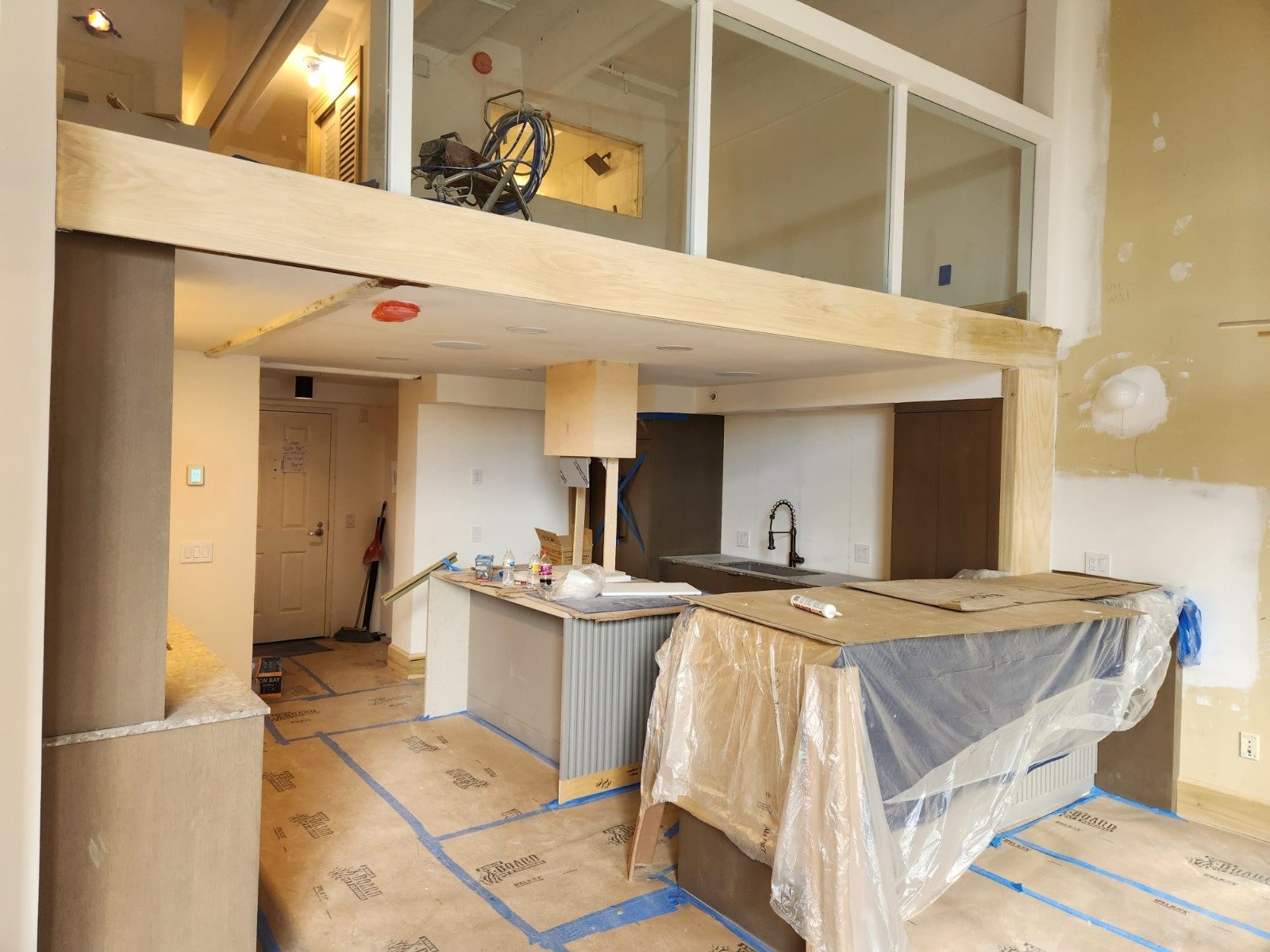 Kitchen wall opened up during a layout change, cabinets protected in plastic