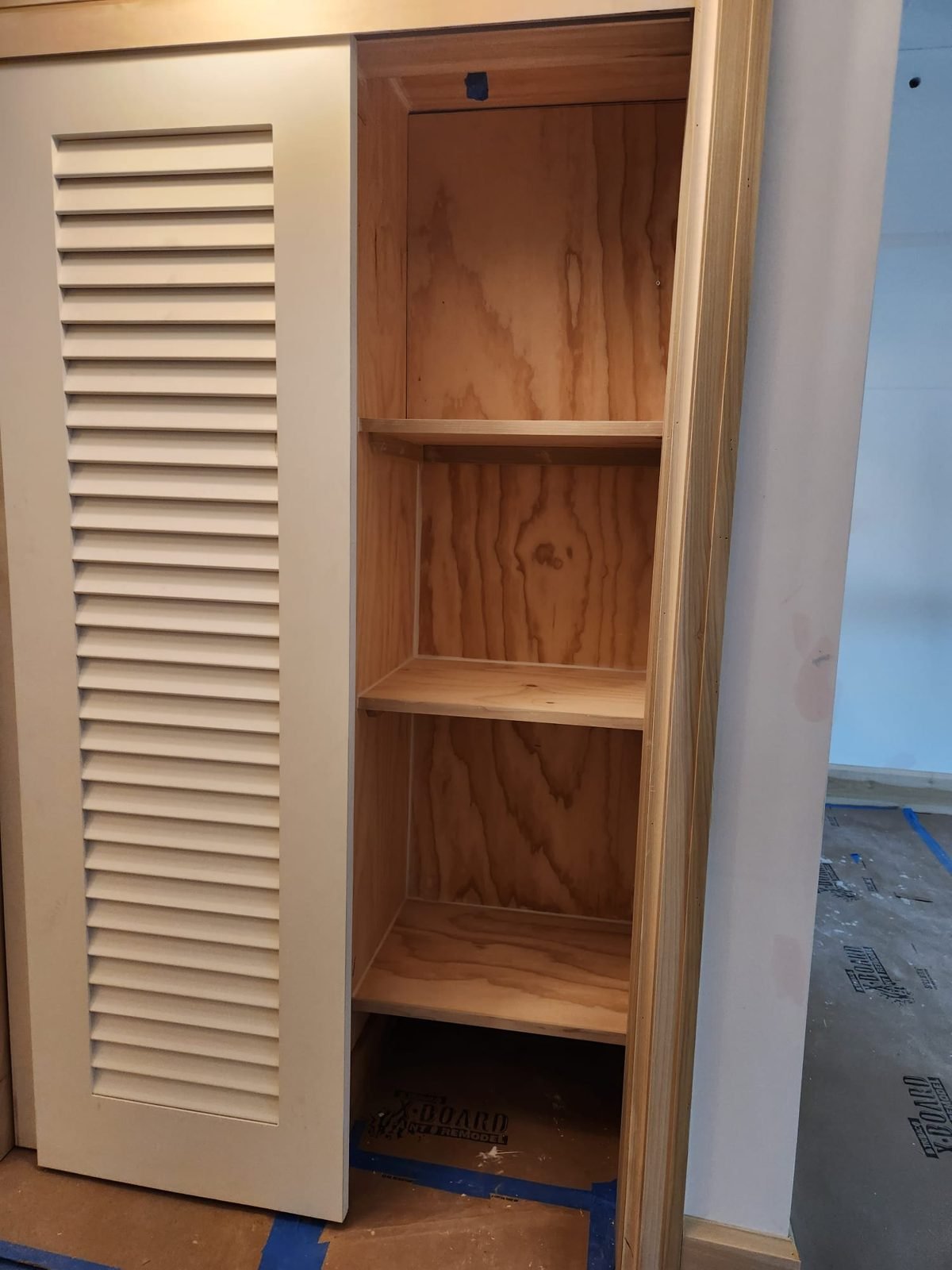 Built-in pantry cabinet with wood shelves and a louvered door