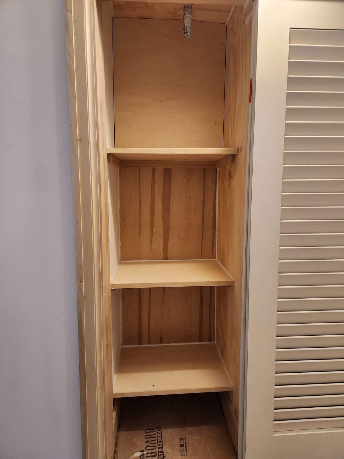 Built-in pantry shelving framed in wood behind a louvered door