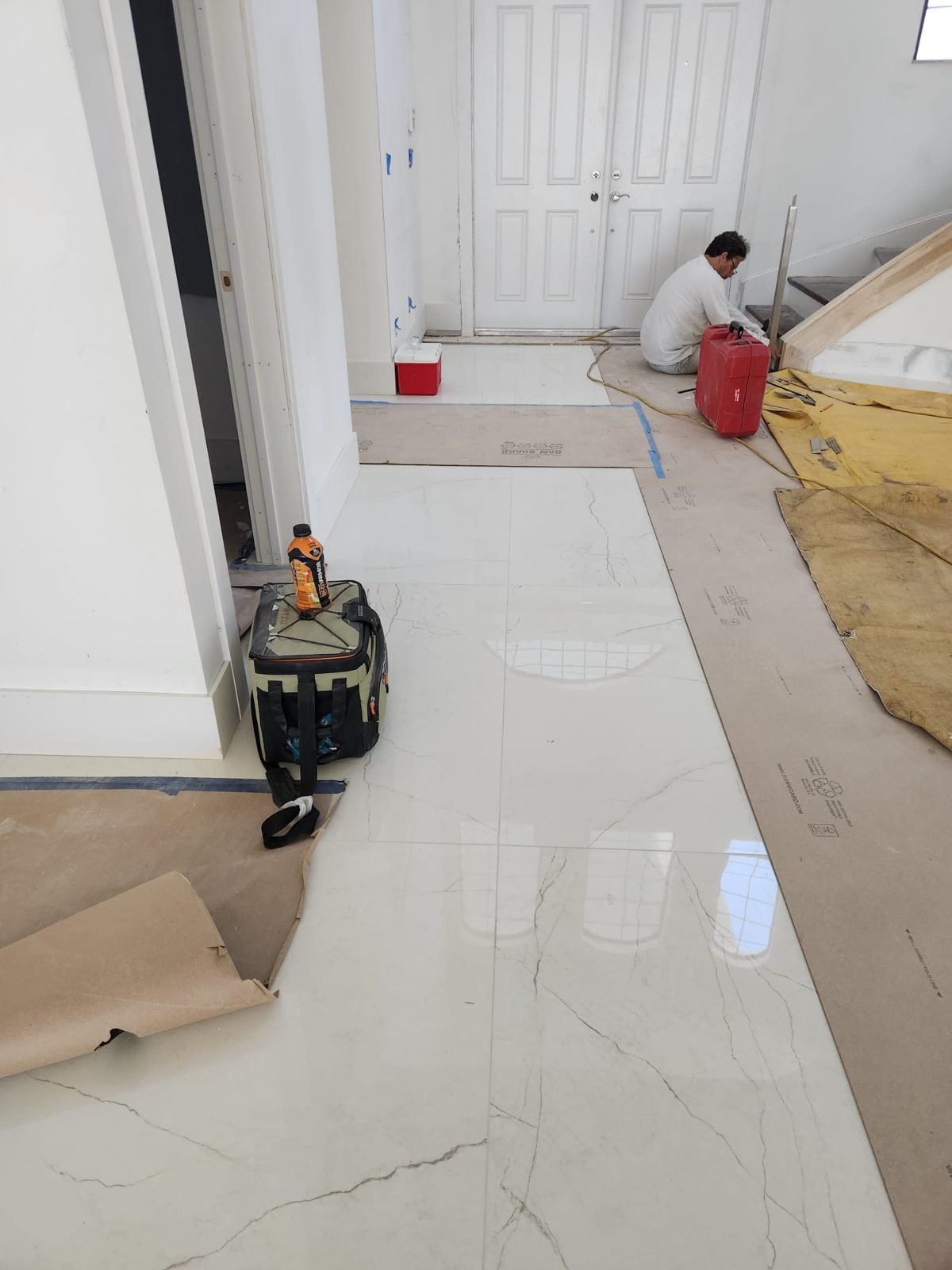 Installer setting large-format marble-look porcelain floor tile in a hallway