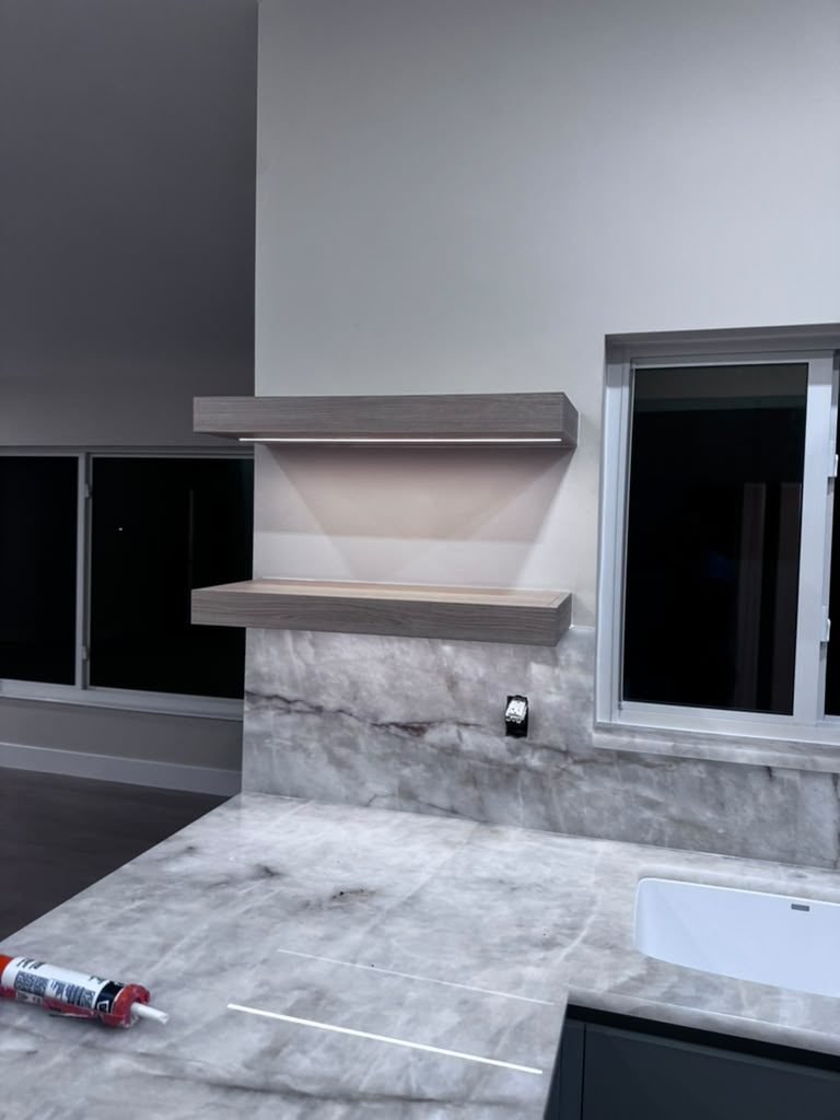 Marble-look countertop and floating shelves being installed along a kitchen window wall