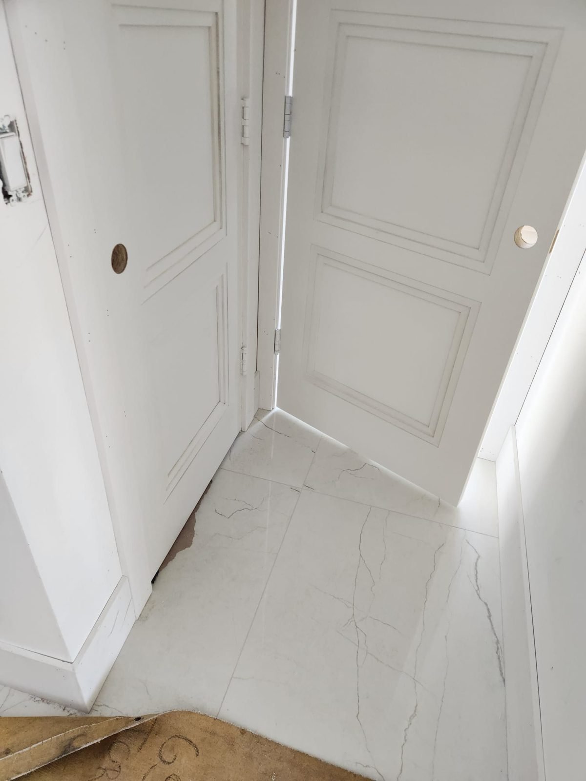 White marble-look tile floor laid through a hallway between panel doors
